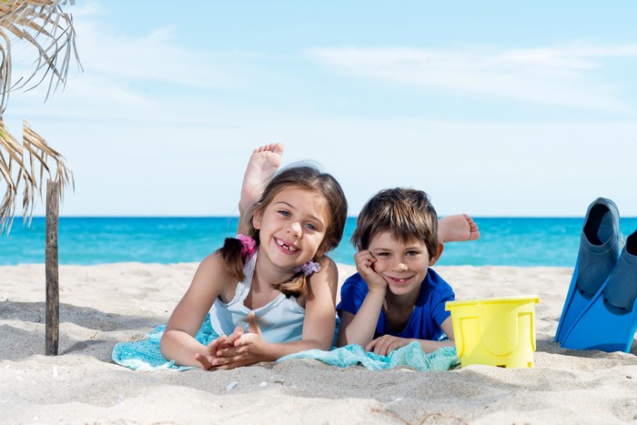 Two children smiling on a beach with flippers and bucket