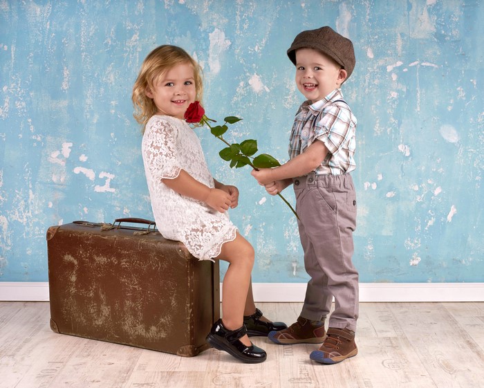 Boy gives a rose to a girl sitting on a suitcase
