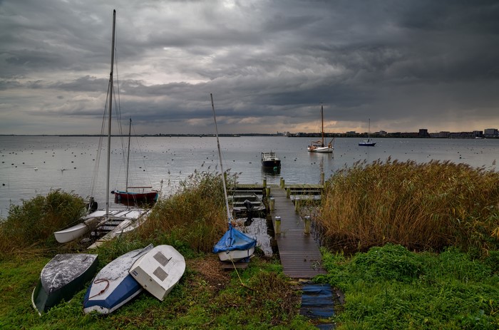 Boats docked by a wooden pier under a cloudy sky