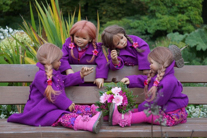 Four dolls sitting on a park bench with flowers