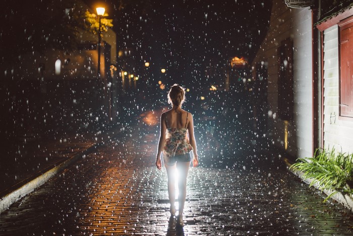 Woman walking in the rain at night on a cobblestone street