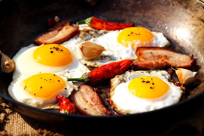Fried eggs with bacon, chili peppers, and garlic in a pan