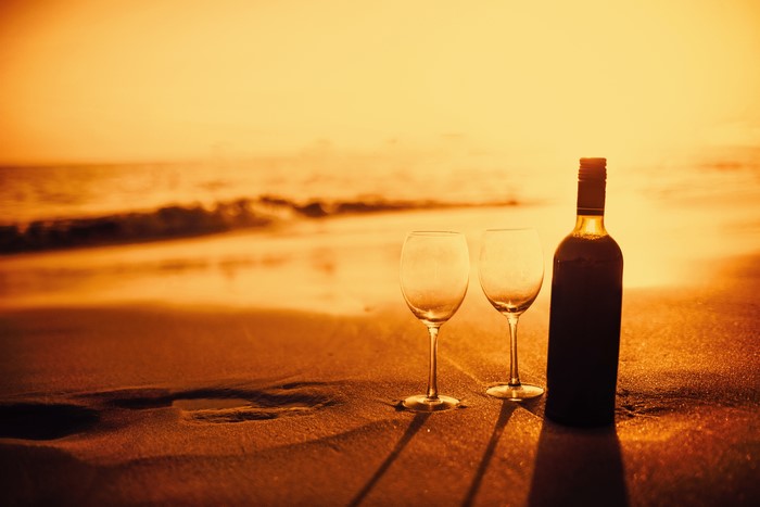 Wine bottle and glasses on a beach at sunset