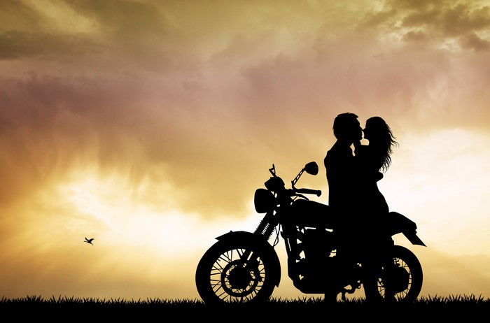Couple kissing on a motorcycle at sunset