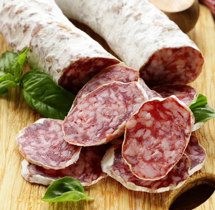 Sliced cured sausage with basil on a wooden board