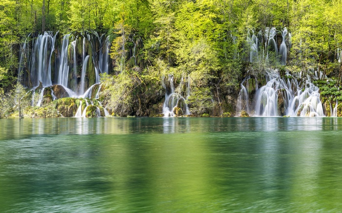 Waterfalls cascading into a green lake surrounded by trees