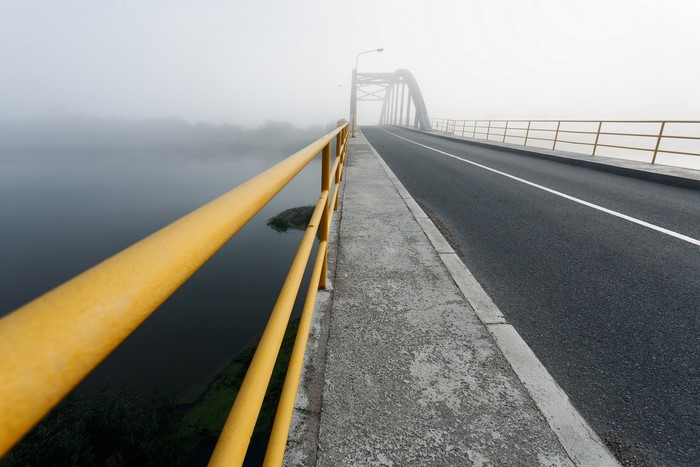 Bridge over water in fog with yellow railing
