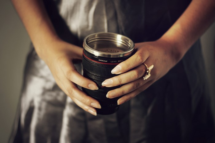 Hands holding a camera lens mug with a ring