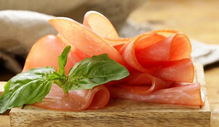Thinly sliced ham with basil on a wooden board