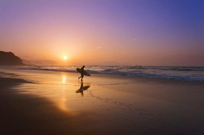 Surfer walking on beach at sunset