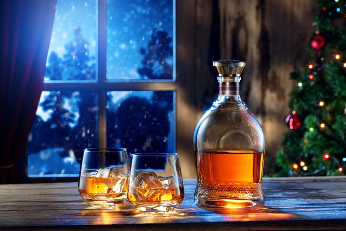 Whisky bottle and glasses by a snowy window and Christmas tree