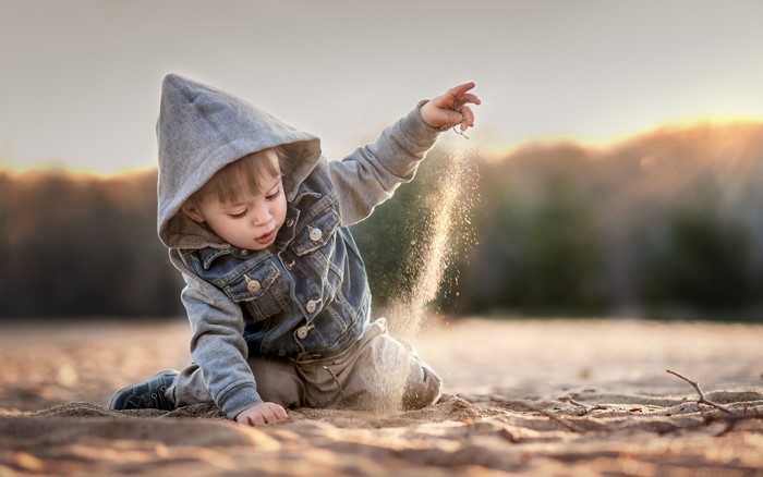 Boy in hooded jacket playing with sand on a beach