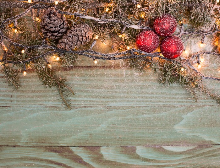 Christmas branches with pine cones, ornaments, and fairy lights on wood