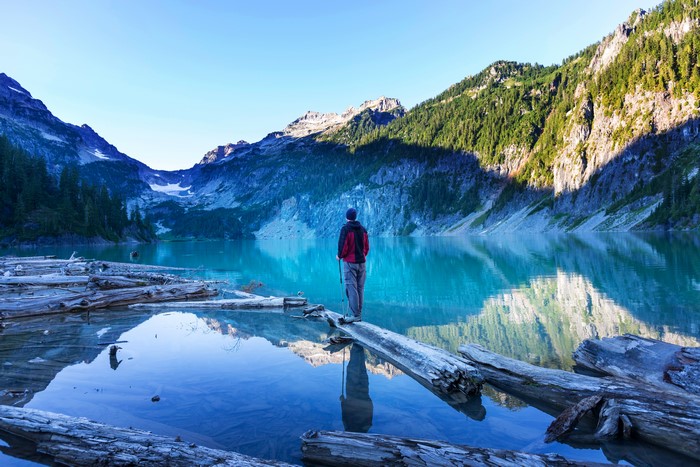Man standing on logs in a lake with mountains