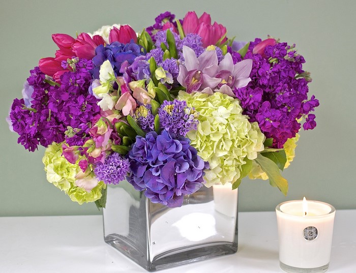 Floral arrangement with hydrangeas, orchids, and tulips in a glass vase with a candle