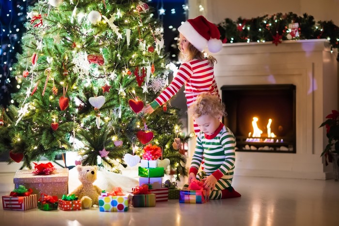 Children opening Christmas gifts by a decorated tree and fireplace