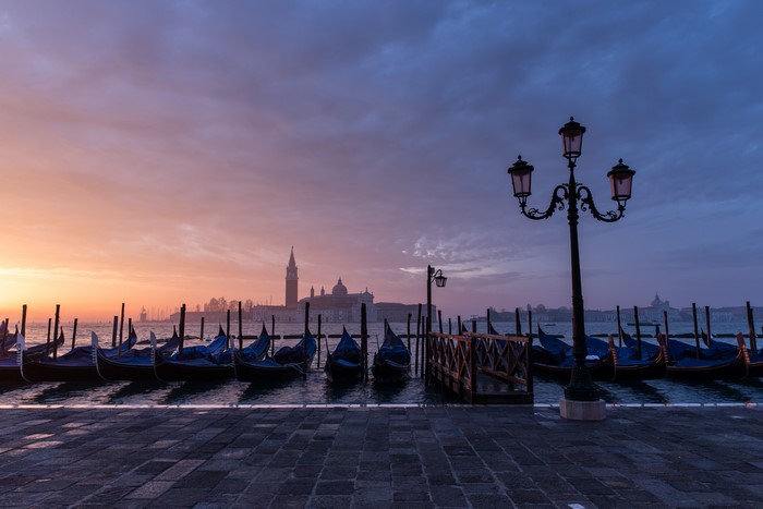 Venice waterfront with gondolas and street lights at sunset