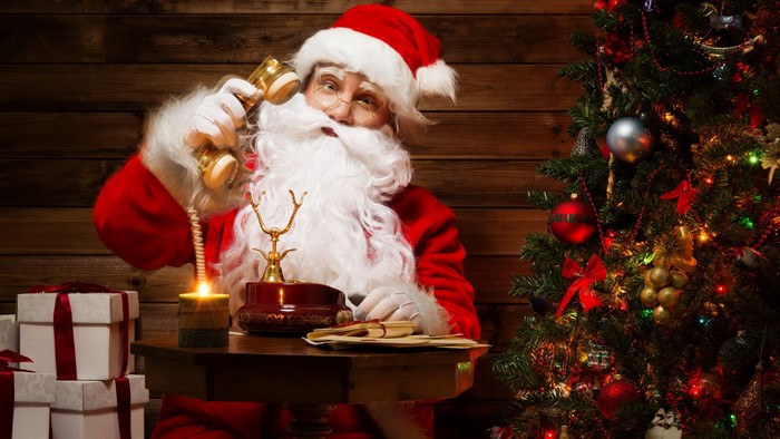 Santa Claus talking on a vintage telephone by a Christmas tree