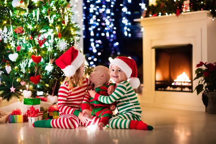 Three Children in Christmas Pajamas by Tree and Fireplace