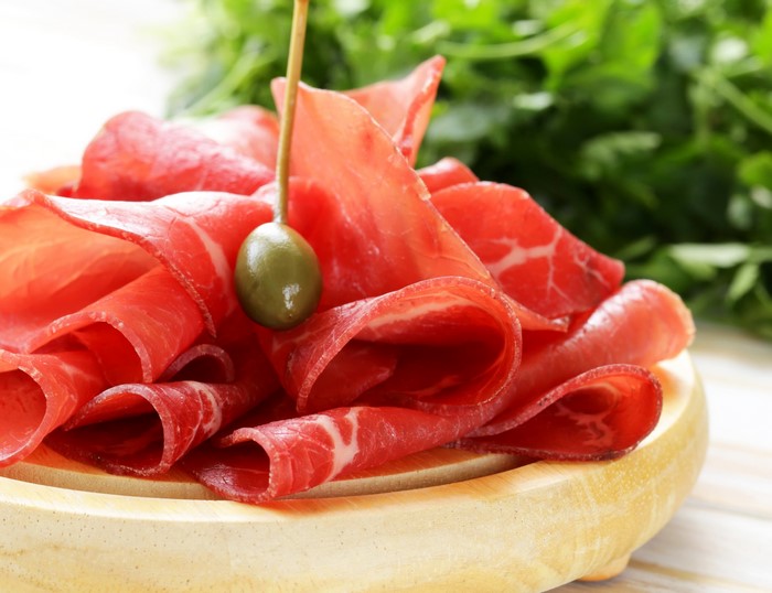Thinly sliced cured meat with a caper on a skewer