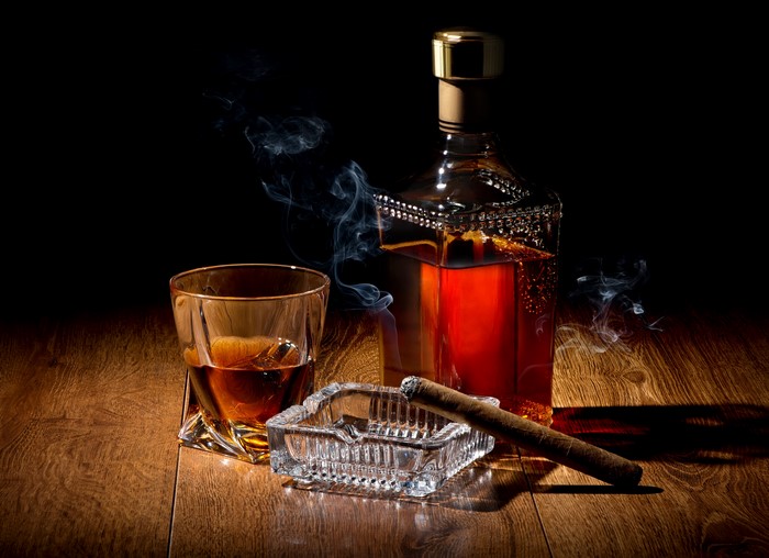 Whisky bottle, glass, ashtray, and cigar with smoke