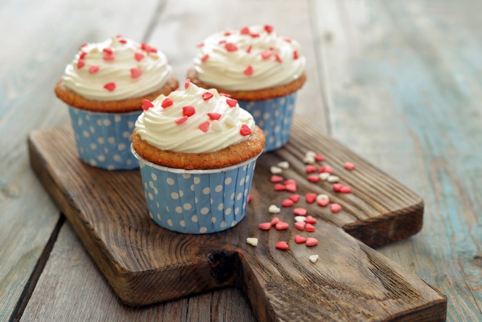 Cupcakes with white frosting and heart sprinkles on a cutting board
