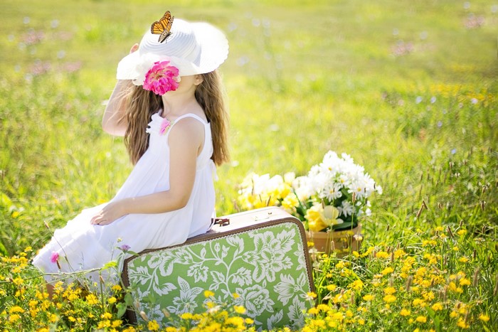 Girl in Hat Sitting on Suitcase in Grasslands
