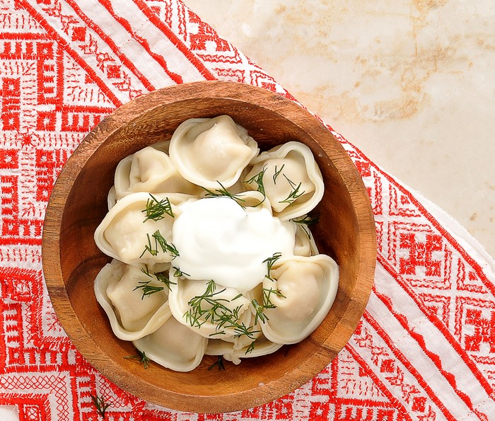 Pelmeni with sour cream and dill in a wooden bowl