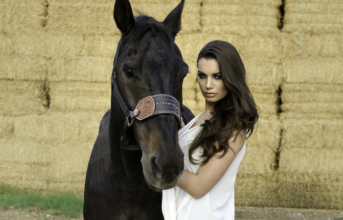 Brunette girl with a black horse in front of hay bales