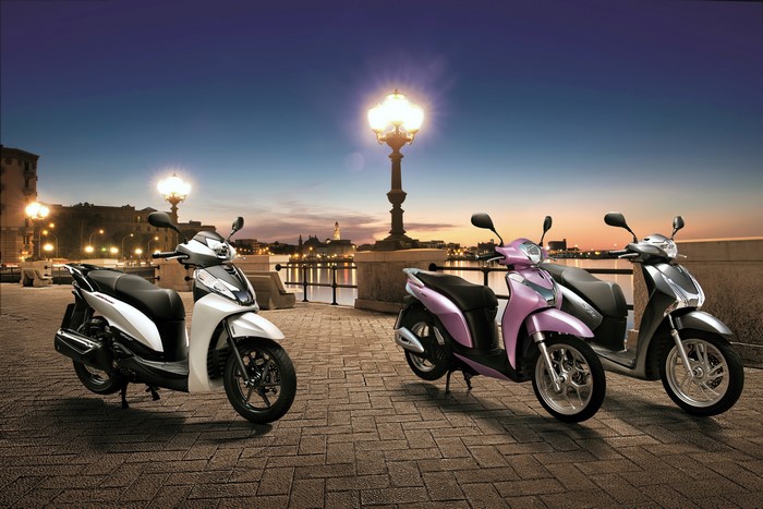 Three Honda scooters on a waterfront at dusk