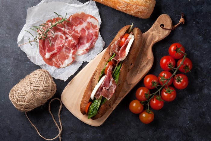 Sandwich with ham, tomatoes, and mozzarella on a cutting board