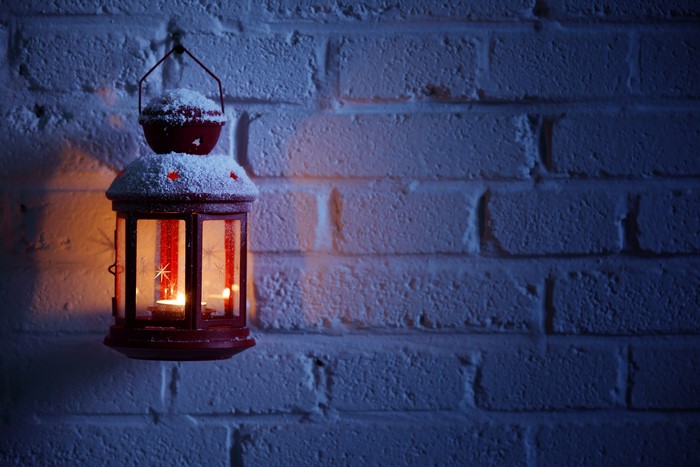 Red lantern with candles on a snowy brick wall at night