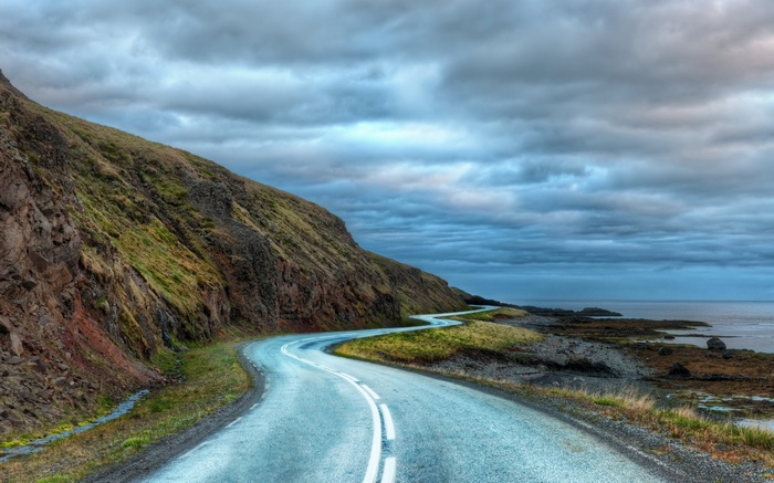 Winding road along a rocky coastline under cloudy sky