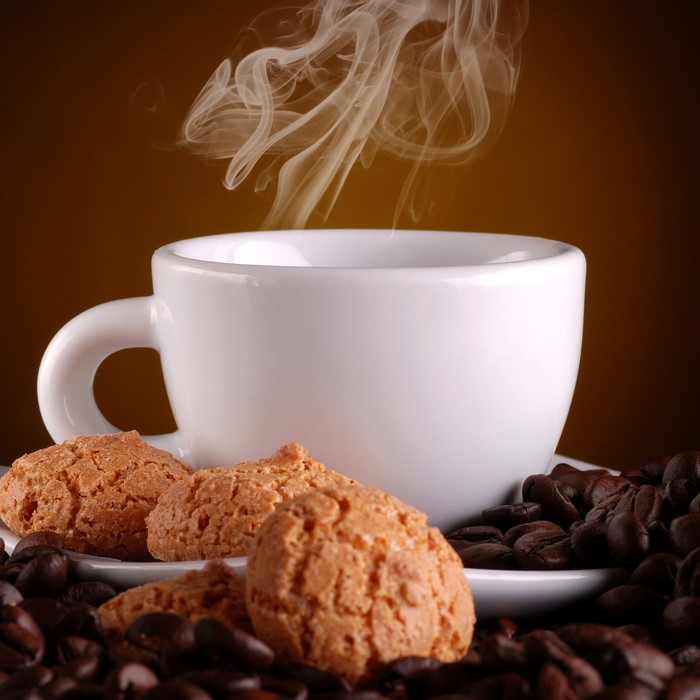 Steaming cup of coffee with cookies and coffee beans