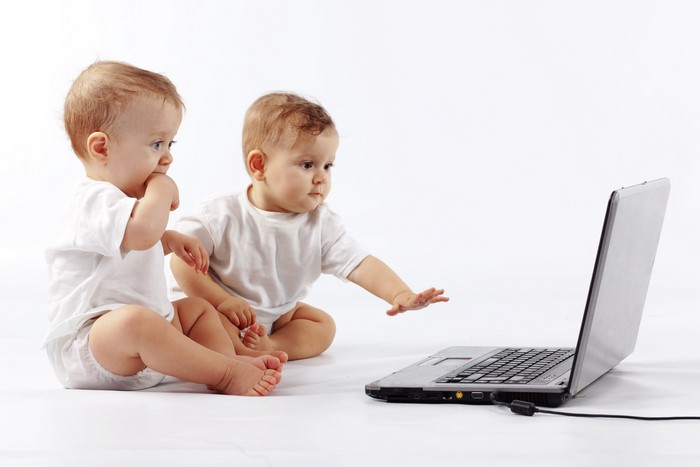 Two infants looking at a laptop on a white background