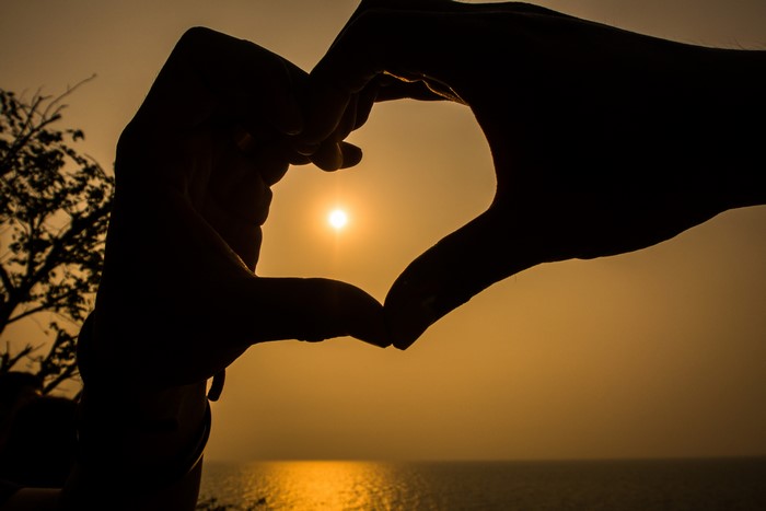 Hands forming a heart silhouette at sunset