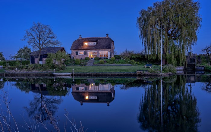 Thatched house and weeping willow by river at dusk, Netherlands