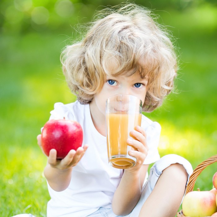 Blonde girl drinking juice and holding an apple