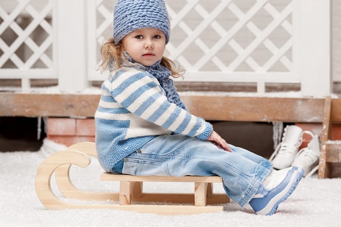 Little girl in winter clothes sitting on a sled