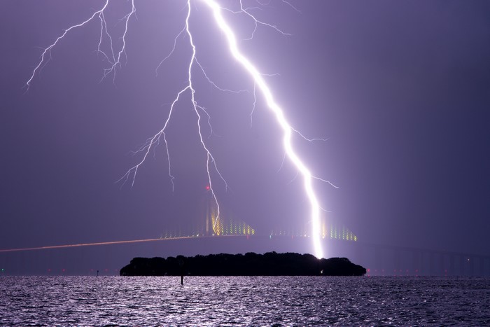 Lightning strikes over water and a bridge