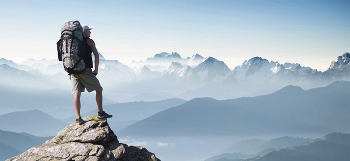 Man with backpack on mountain peak overlooking ranges