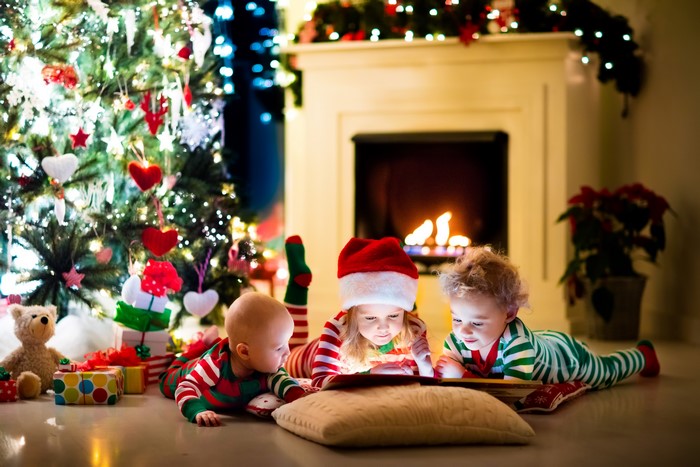 Three children reading a book by the fireplace and Christmas tree
