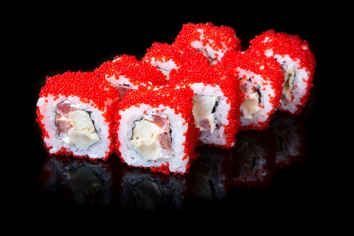 Sushi rolls with red caviar on black background