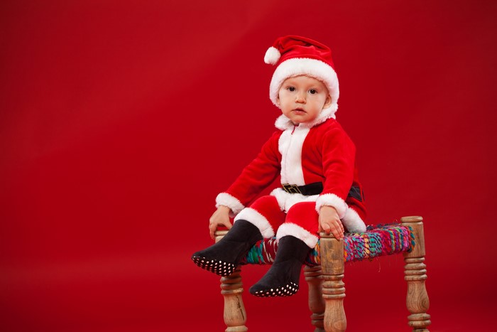 Baby in Santa Claus costume sitting on a stool