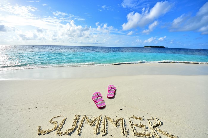 Summer written in sand on a beach with flip-flops