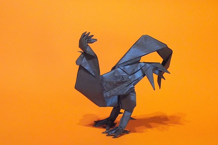 Origami black rooster on an orange background
