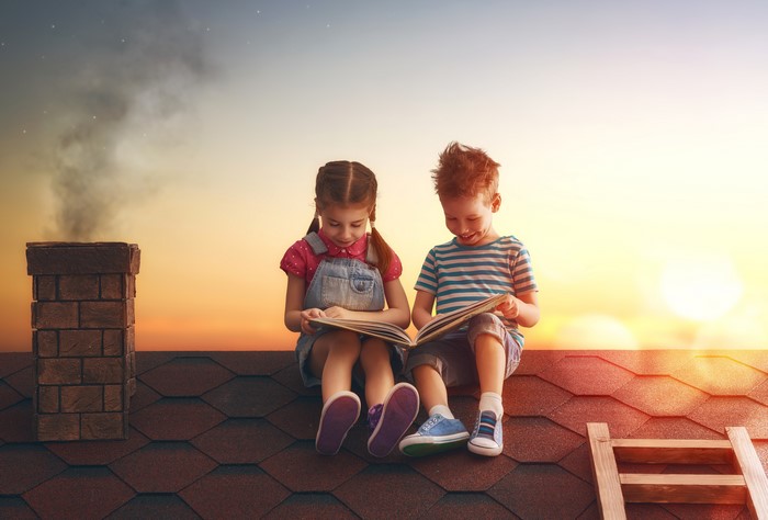 Two children reading books on a rooftop at sunset