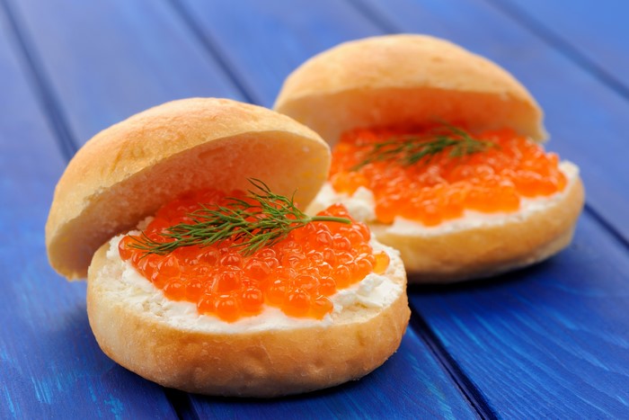 Buns with cream cheese and red caviar on blue wooden planks