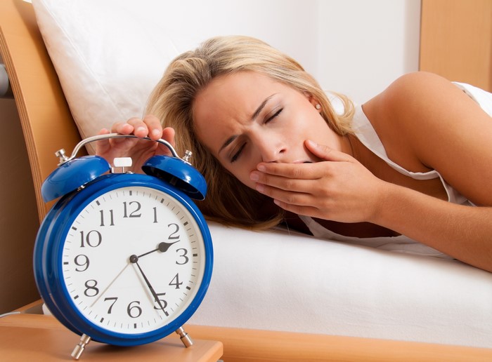 Woman yawning next to an alarm clock