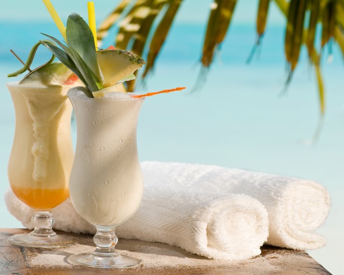 Two tropical cocktails with pineapple and towels on a beach